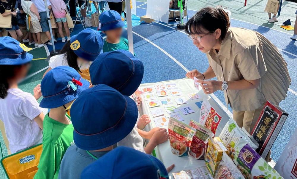 第19回北区環境展当日の様子。 ブースに集まる小学生に、ヴィーガンについて紹介するベジプロジェクトジャパンのスタッフ