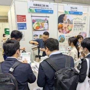 プレミアム・フードショー2025のヴィーガンセレクションで、丸善食品工業株式会社のブースに集まる来場者