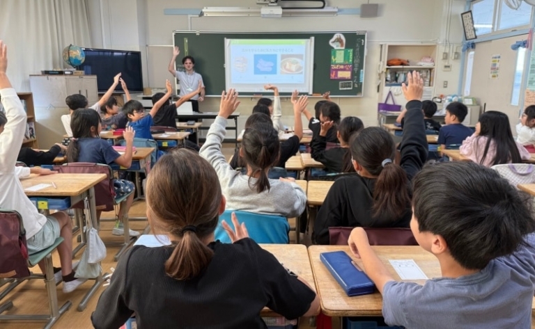 Students raising their hands in a classroom while a VegeProject Japan instructor speaks at the front